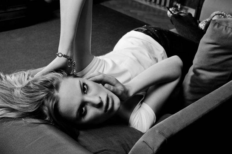 Black and white: a blonde woman lies on a sofa with her hand by her face.