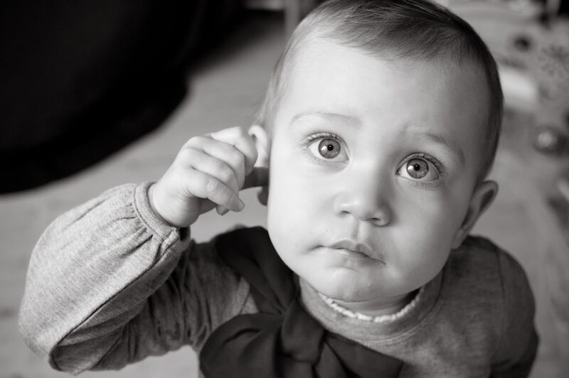 Black and white: a young child holds a hand to their ear and looks up curiously.