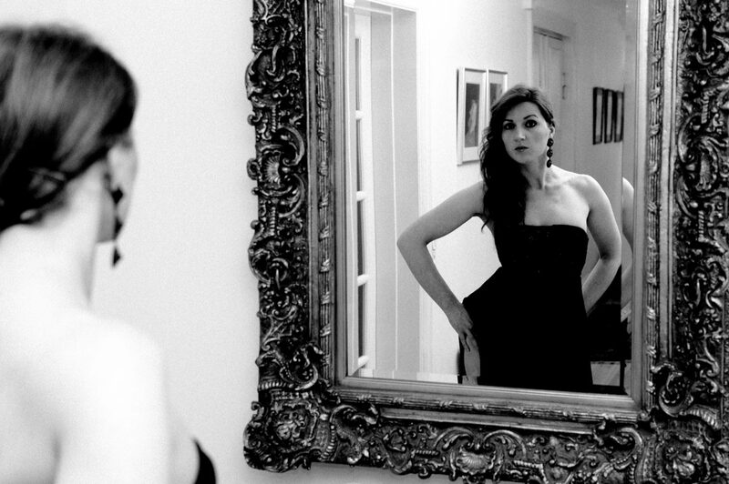 Black and white: a woman in a strapless dress is reflected in an ornate mirror.