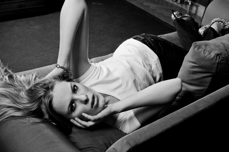 Black and white: a blonde woman lies upside down on a sofa, her hand under her chin.