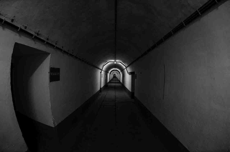 A long, curved concrete tunnel inside Fort Eben-Emael fades into a pale light at the end.
