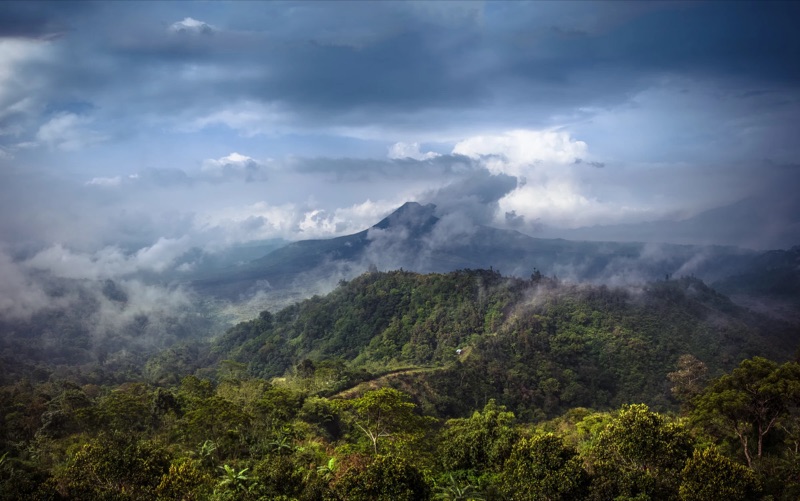 Clouds drift over forested mountains under a blue-grey sky.