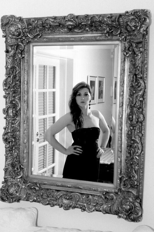 Black and white: a woman in a strapless dress poses inside the frame of an ornate mirror.