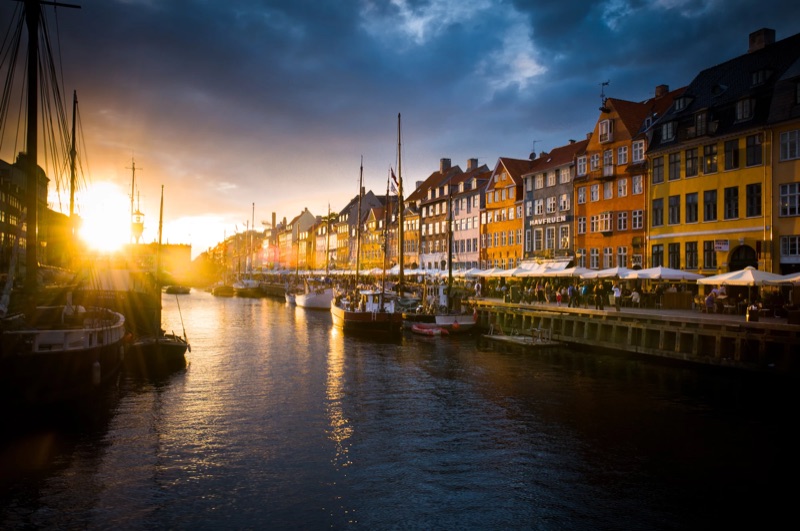 The sun sets behind boats and colourful houses along the Nyhavn canal.