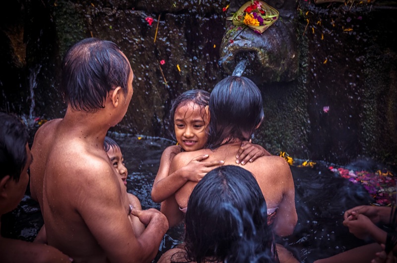 A father holds his smiling daughter in the holy spring water of Tirta Empul temple.