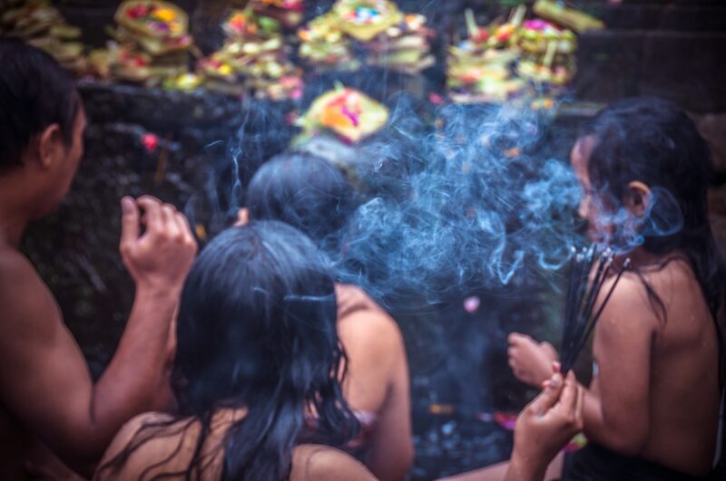 Worshippers pray in incense smoke in front of flower offerings at Tirta Empul.